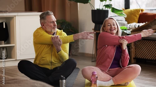 Happy middle-aged couple in activewear stretching arms during home workout