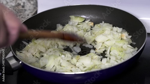 Chopped onions are being cooked in a pan on the stove. A hand stirs the onions, making them soft and golden. This is a common step in many recipes.