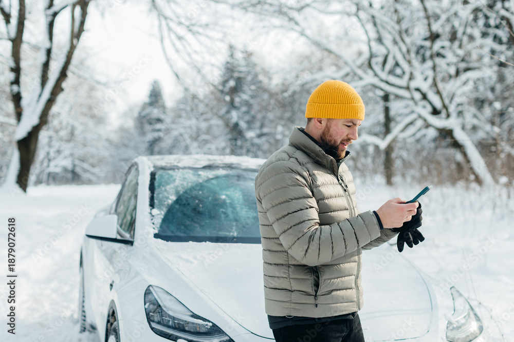 Naklejka premium Driver checking smartphone near electric car in winter