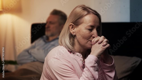 Upset middle-aged woman and her husband sitting apart on bed, divorce concept