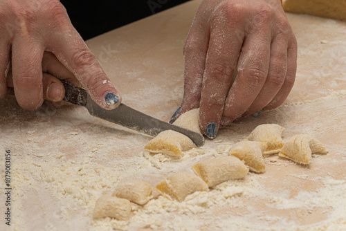 Hands cutting fresh homemade gnocchi on floured board, perfect for Italian cooking tutorials, recipe blogs, restaurant branding, artisanal food stories, and rustic cuisine visuals