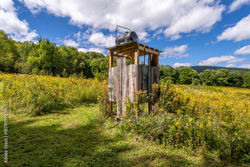 Canvastavla Rustic outdoor shower in wildflower meadow with wooden enclosure and blue sky in