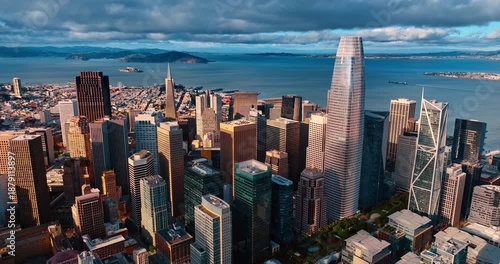 Moving over the tops of high-rises approaching the highest skyscraper. Salesforce Tower in the downtown of San Francisco, CA, USA. Dramatic cloudscape over the waterscape ta backdrop.