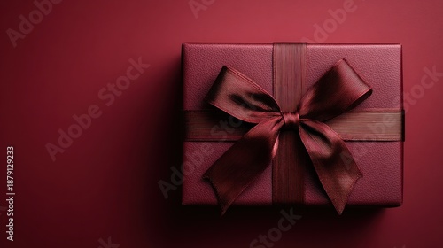 A festive, wrapped gift box is presented. The box is adorned with an elegant ribbon and tied in a bow. It has a classic deep red color for the holidays