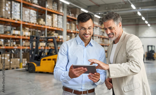 Obraz na płótnie Team of two happy professional warehouse managers working standing in storage using digital tablet
