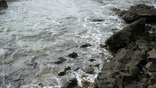 Ocean waves crashing against dark coastal rocks creating natural sea foam