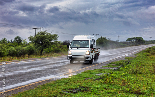White light commercial truck with a flatbed drives on a rain-slicked highway during a storm