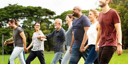 Diverse group of friends hold hands at park. Diverse group of men and women standing together hold hands at park. Diverse group of friends, men and women, standing in row hold hands on grass.