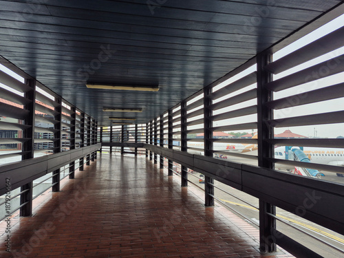 Classic airport terminal connecting corridor with wooden ceiling, ventilated wooden walls, and brown tile floor, designed for natural airflow, comfort, and traditional architectural style.