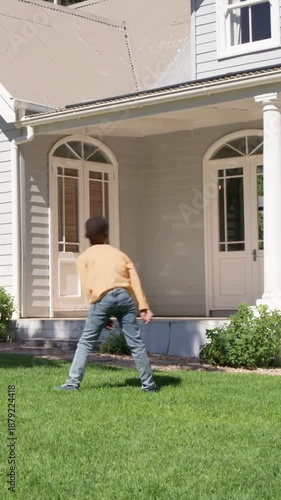 Vertical video: Feinting dad training son in yellow top dribbling soccer ball to goal on front lawn