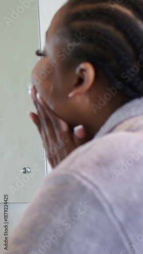 Vertical video: Glancing into mirror woman in robe rubbing jaw checking skin at sink, copy space