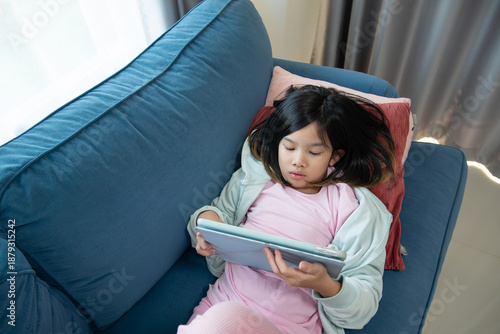 Cuadro en lienzo Young Asian Girl Relaxing on a Sofa and Playing or Watching a Tablet Computer