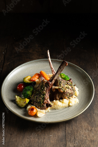 Herb-Crusted Lamb Rack with Mashed Potatoes and Roasted Vegetables on Dark Rustic Background
