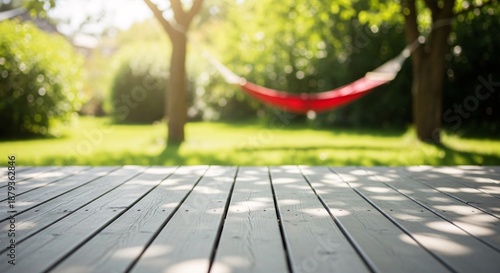 Relaxing outdoor scene featuring a vibrant red hammock suspended between two lush green trees on a sunny day with a wooden deck in the foreground and a peaceful garden background