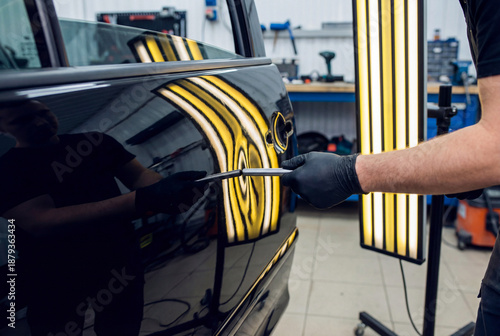 PDR specialist using metal tool to fix car door dent checking reflection in striped line board