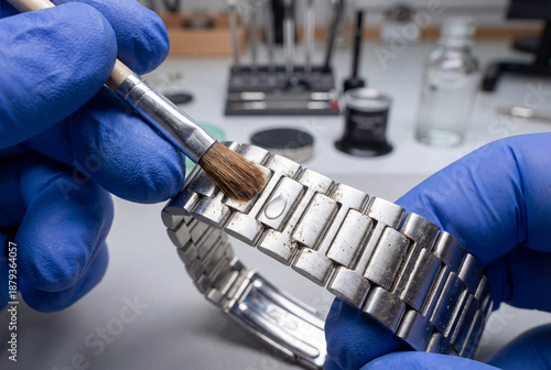 eweler hand in blue glove cleaning metal watch bracelet links with brush removing dirt macro