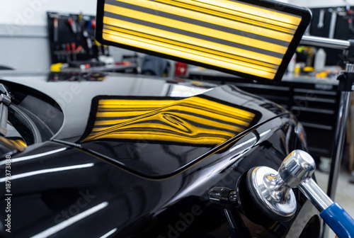 Specialist performing paintless dent repair PDR on car door checking reflection in line board