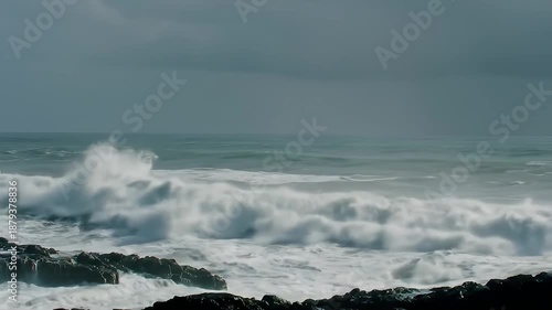 Dramatic Ocean Waves Crashing on Rocky Shoreline Under Moody Stormy Skies with White Foam and Spray in Natural Lighting