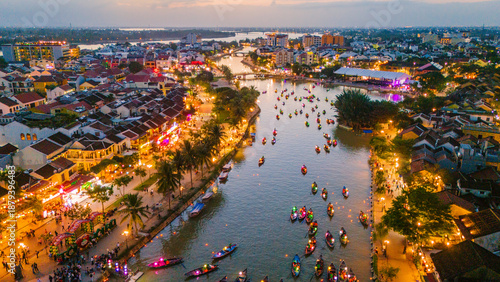 aerial view of the historic Hoi An Ancient Town at sunset, featuring the Thu Bon River filled with colorful lantern boats and the illuminated streets of the UNESCO World Heritage site