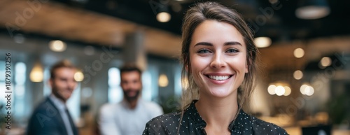 Smiling young woman standing in modern office with colleagues behind  