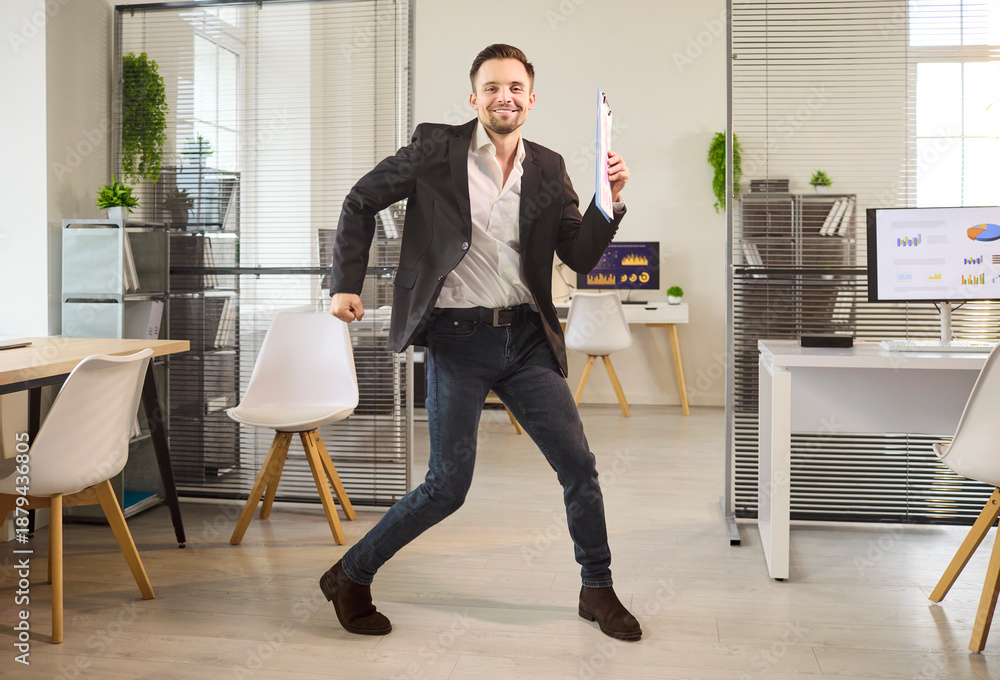 Fototapeta premium Businessman office success happy dance celebration victory. He celebrates growth with reports in a workspace, symbolizing profit, motivation and achievement. Clear concept of victory and joy.