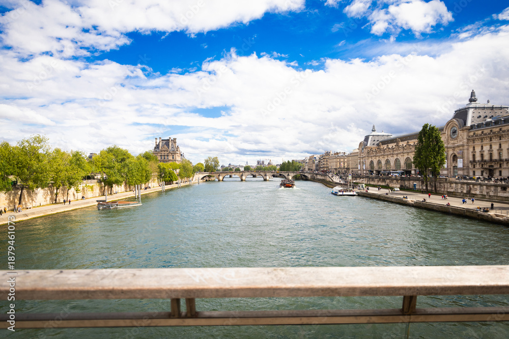 Fototapeta premium View of Seine River with buildings along the bank and boats sailing on a sunny day in Paris