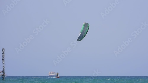 Kiteboarding and kitesurfing as a kiter is pulled across sea water by a power kite. Kiteboarders and kitesurfers ride wind power near the beach for extreme sea sport.