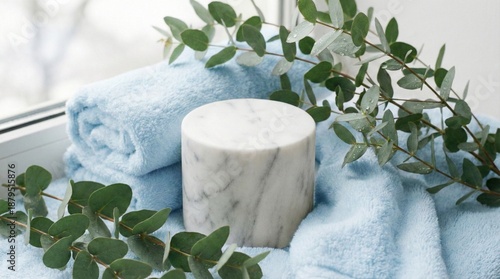 Marble cylinder podium on blue towel with eucalyptus branches. Bathroom product display background
