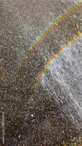 A rainbow over the spray from an outdoor shower during the day; Vertical; Video