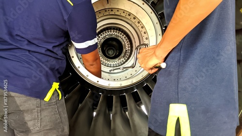 Aircraft maintenance technicians performing detailed inspection and maintenance on a turbofan jet engine inside an aircraft hangar