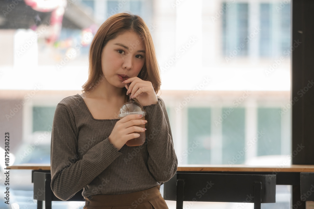 Obraz premium Asian woman drinking an iced coffee.