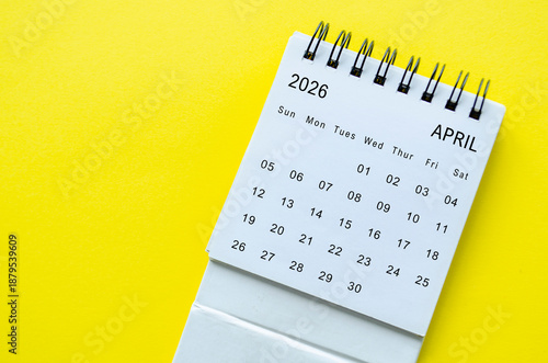 White spiral desk calendar for April 2026 on yellow background with minimal layout and space for text.