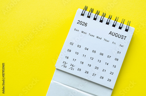 White spiral desk calendar for August 2026 on yellow background with clean composition and space for text.