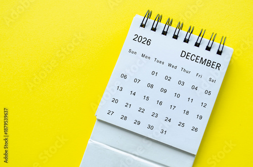 White spiral desk calendar for December 2026 on yellow background with simple design and space for text.