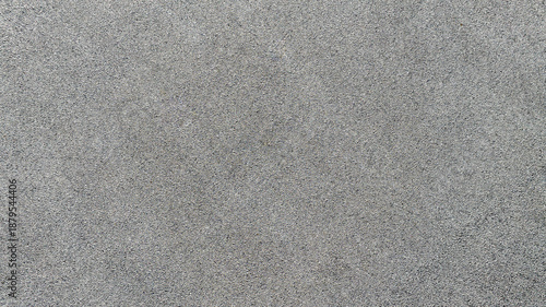 High-angle shot of a dark grey asphalt surface. The fine, grainy texture provides a uniform and neutral background, ideal for urban and industrial design themes, pattern and backgrounds. Zenith view.