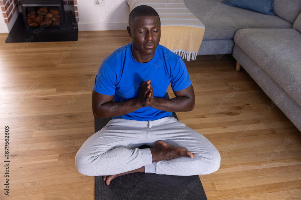 Fototapeta premium African american man meditating cross-legged on yoga mat in hall with fireplace logs