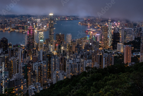 Viewed From Victoria Peak Over Hong Kong Night Skyline With Illuminated Skyscrapers And Dense Cityscape