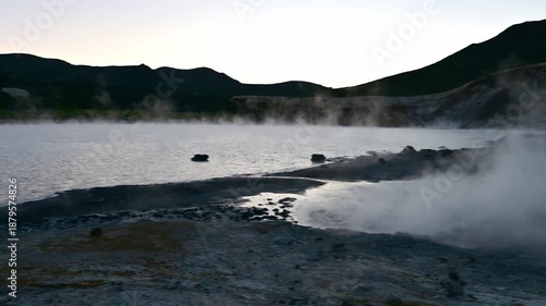 Nature's raw beauty unfolds as steam rises from a sulfur field and geyser on Kunashir Island. Witness the volcanic landscape in the stunning Kuril Islands at dusk.