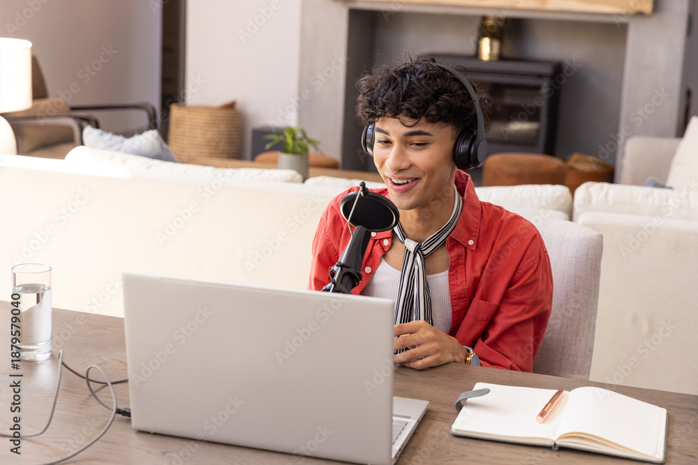 Fototapeta premium Man recording podcast using laptop, microphone and headphones in living room with notebook