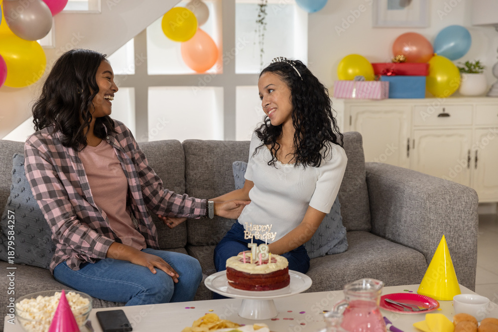 Obraz premium Diverse mom and teenage daughter sitting on sofa celebrating 18th birthday with red velvet cake