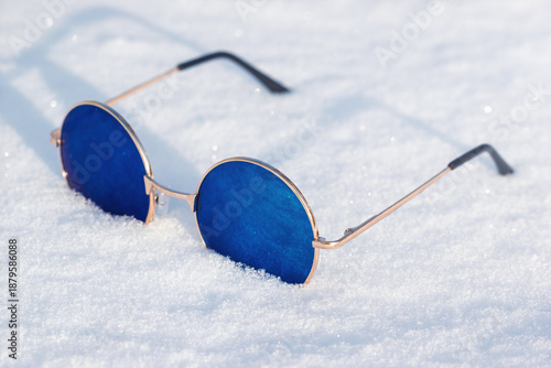 Cool hippie blue lens sunglasses on the bright white snow. The eye protection in winter season.