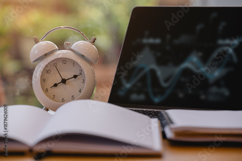 Alarm clock with laptop and notebook on wood desk, calculator and notebook on desk representing time management, productivity, deadlines and business planning concept