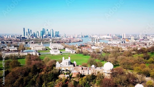 Aerial drone shot elevating above Royal Greenwich Observatory, revealing Isle of Dogs and Canary Wharf skyline, modern skyscrapers, sunny day, blue sky, cinematic London cityscape