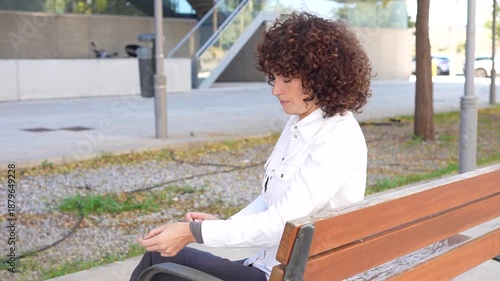 A Thoughtful Young Woman Wearing Stylish Attire Sitting on a Park Bench in Daylight