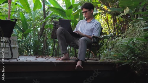 Young Asian businessman talking and working on a laptop while sitting in a lush green garden cafe