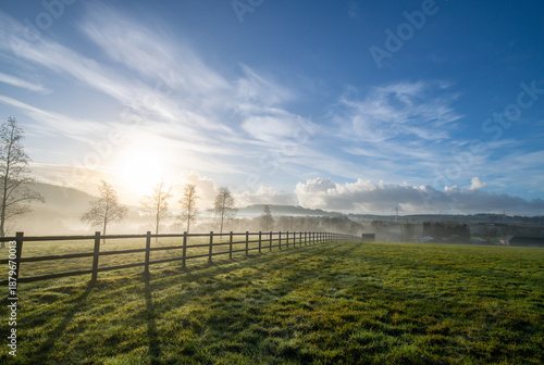 English countryside picture showing a green field at sunrise with a wooden fence acting as a strong leading line. Vibrant blue sky adds to to rural lifestyle and country life feel.