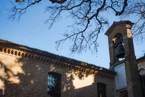 Historic brick building in Ravenna with a bronze bell gable and marble plaque under bare winter tree branches
