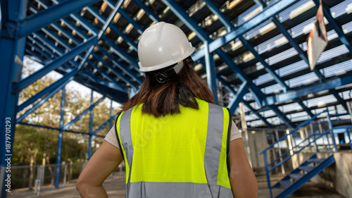 Slika na platnu A person wearing a hard hat and safety vest stands at a construction site