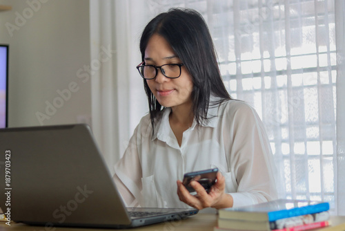 Asian woman in white shirt sitting at a desk with a laptop and a tablet to online learning , shopping for technology concept