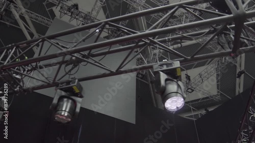 Moving spotlights emit sharp beams illuminating hanging LED panel. Lighting flickers rhythmically revealing concert system synchronization
